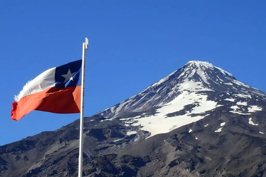在智利和阿根廷之间的陆路边境上，一座被雪覆盖的火山和一面智利国旗