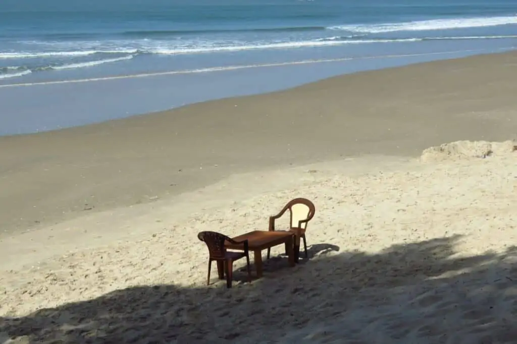 海边的沙滩上有一张桌子和两把棕色的塑料椅子