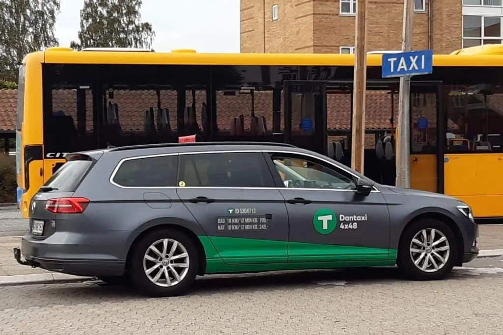 一辆灰色和绿色相间的丹出租车停在哥本哈根公共汽车旁边。