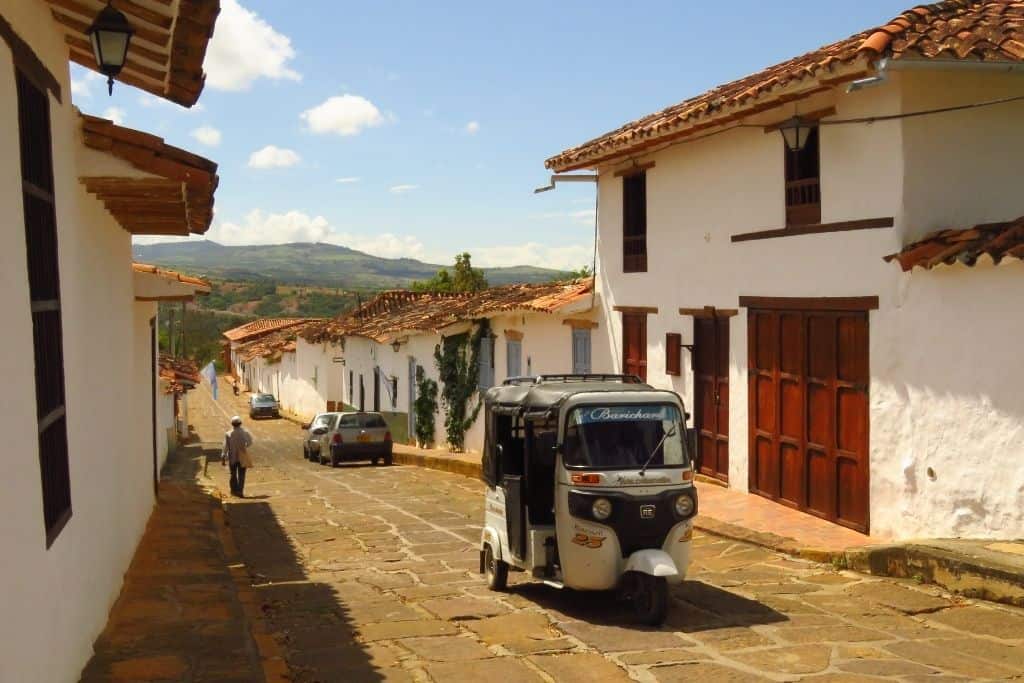 在哥伦比亚的巴里卡拉，白色的房屋和一辆突突车行驶在鹅卵石街道上，远处是丘陵景观。