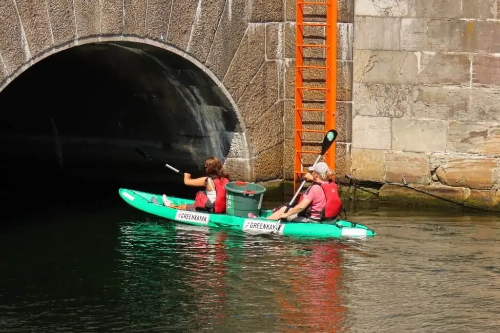 两个女人划着绿色皮艇，准备从哥本哈根的大理石桥下经过
