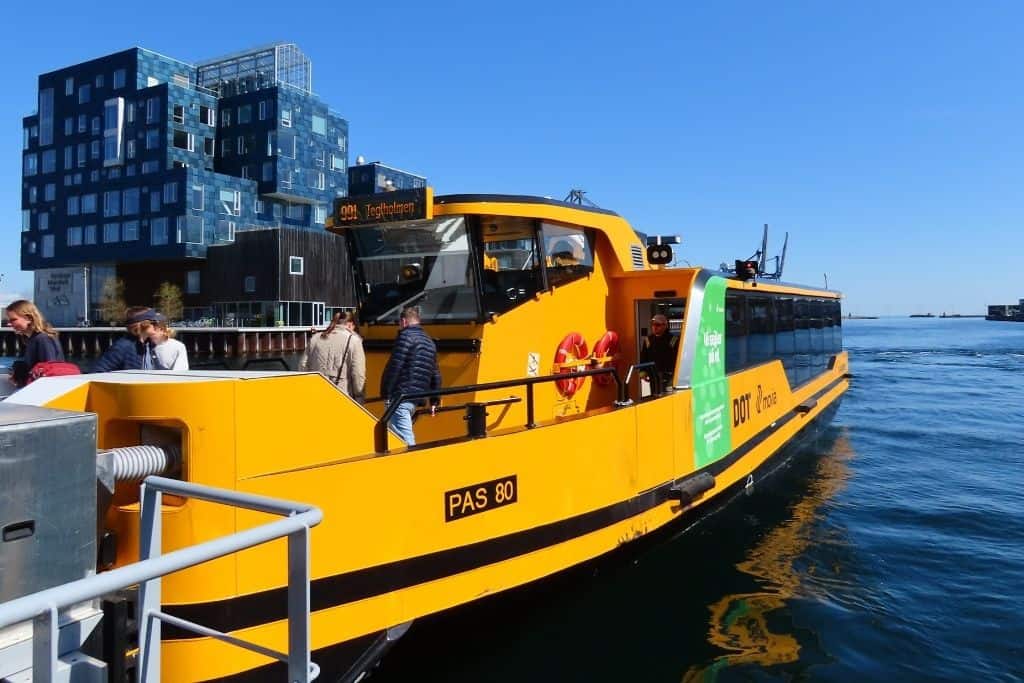 一辆亮黄色的哥本哈根海港巴士在Orientkaj的水面上等待乘客上车。
