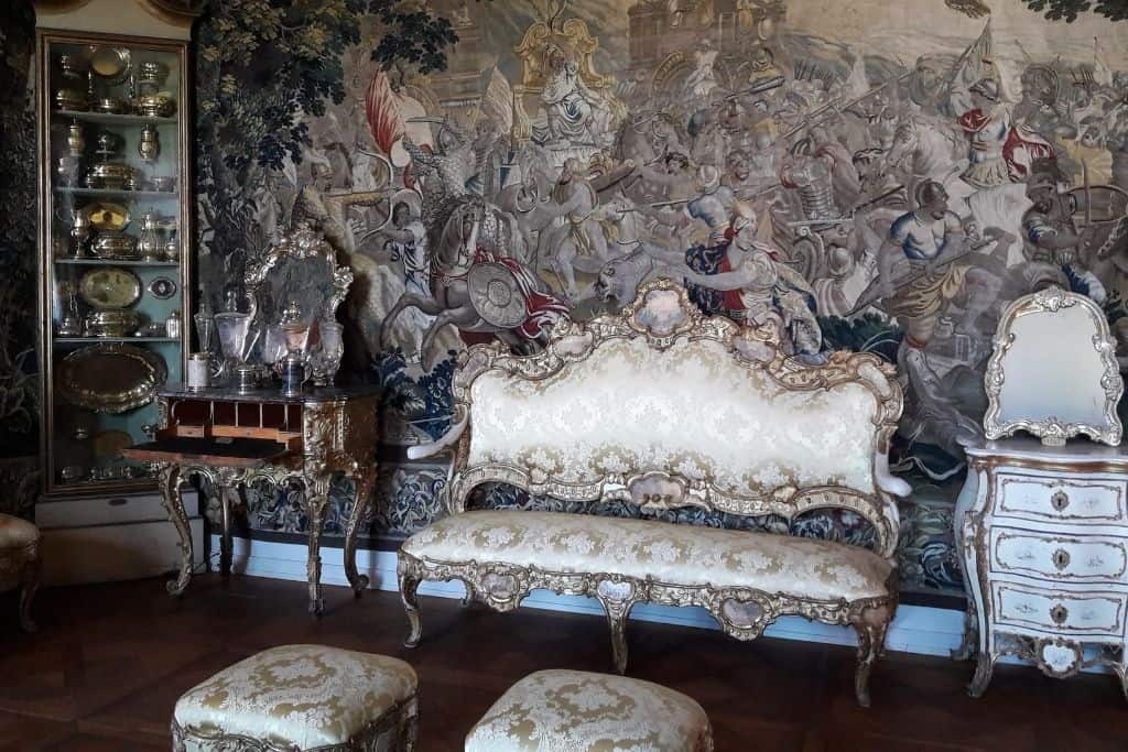 哥本哈根罗森堡城堡内的一个装饰过度的房间，有战争场景的壁画，一个角柜，桌子，沙发，脚凳和梳妆台。