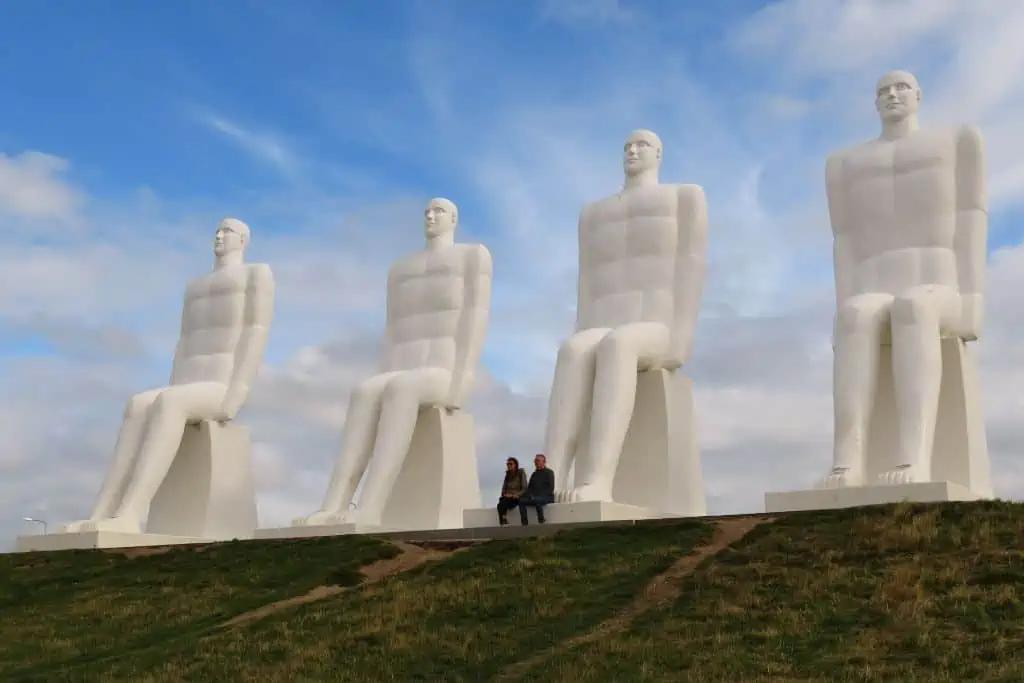 四个人分别坐在长满草的山顶的白色凳子上的巨大白色雕像。