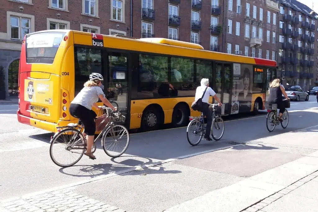 一个黄色的公共汽车停在一个公共汽车站与骑自行车的人路过。
